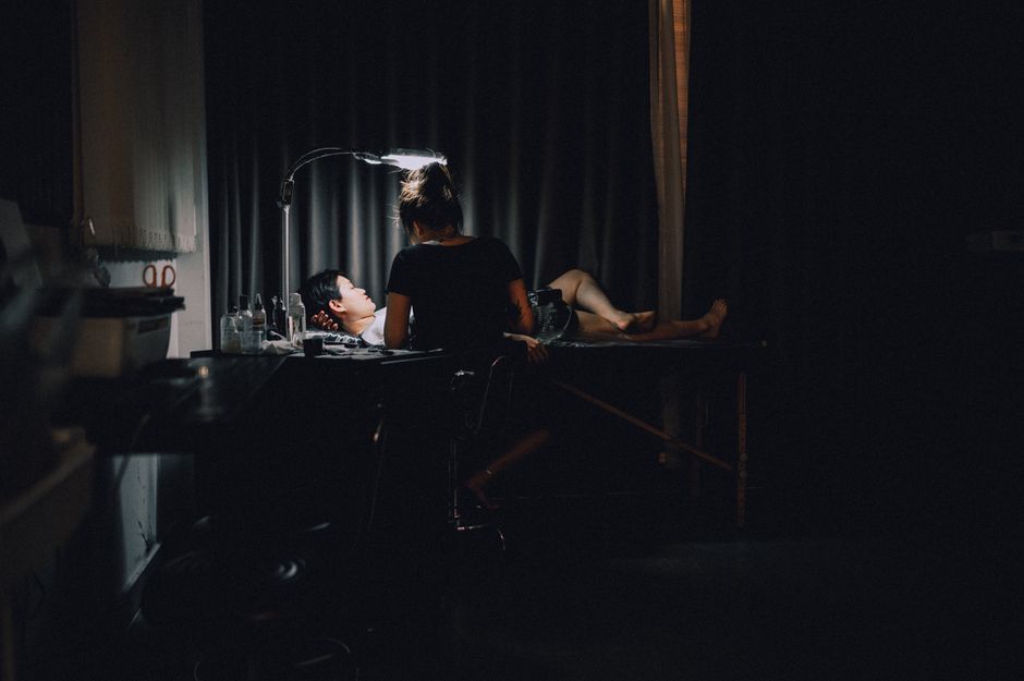 A tattoo artist focused on her work in a dimly lit studio with a client.