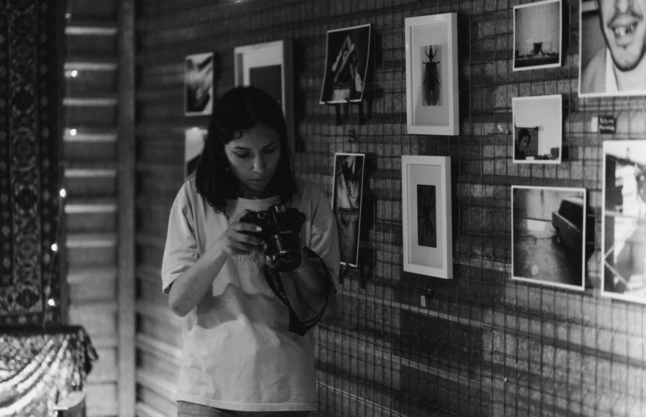 A woman examines her camera in an art gallery with framed photos.