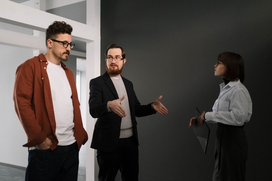 Three colleagues engaged in a project discussion inside an office with a gray wall backdrop.